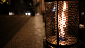 A gas flame in a cylindrical shaped patio heater burning behind a screen.